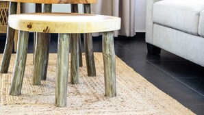 Een ronde houten tafel met een natuurlijke afwerking, rustend op vier houten poten, geplaatst op een rug met een structuur.