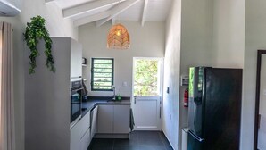 Een keuken met een zwarte koelkast, witte kasten, een hanglamp en een raam met uitzicht op bomen.