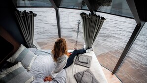 En säng med utsikt över havet, ett glastak och ett fönster med gardiner.