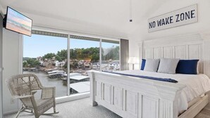 Ein Schlafzimmer mit Bett, Sessel, Fernseher und Blick auf das Wasser.
