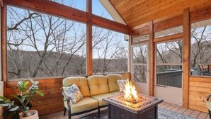 A cozy room with a sofa, a fire pit, and large windows. - Lakefront Near State Park w/ Dock, Kayaks, Bunk Room & Multi-Level Decks (Osage Beach)