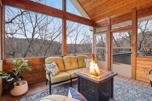 A cozy room with a sofa, a fire pit, and large windows.