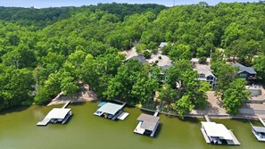 A lakeside property with multiple docked boats, a bridge, and a forested hillside. - Lakefront Near State Park w/ Dock, Kayaks, Bunk Room & Multi-Level Decks (Osage Beach)