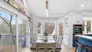 A modern kitchen with white cabinets, a blue countertop, and a dining area with a wooden table and chairs. - Lakefront Near State Park w/ Dock, Kayaks, Bunk Room & Multi-Level Decks (Osage Beach)
