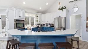 A modern kitchen with white cabinets, a blue island, stainless steel appliances, and a large window. - Lakefront Near State Park w/ Dock, Kayaks, Bunk Room & Multi-Level Decks (Osage Beach)