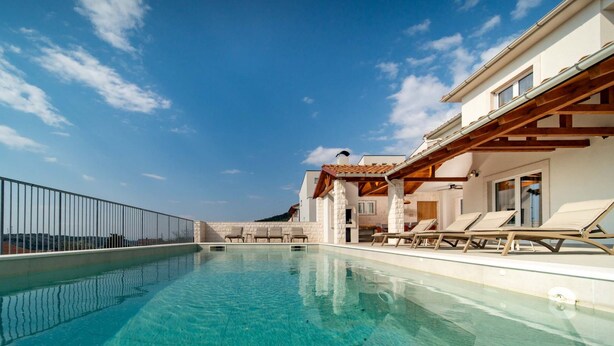 Ein Schwimmbecken mit Liegestühlen, einer überdachten Terrasse und Blick auf die umliegende Landschaft.