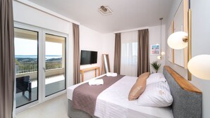 Ein Hotelzimmer mit Bett, Fernseher, Schreibtisch und einem Balkon mit Aussicht.