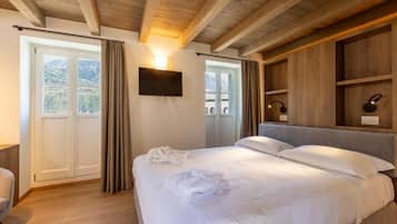 Ein Schlafzimmer mit Bett, Fernseher, Holz-Kopfteil und Blick ins Freie.