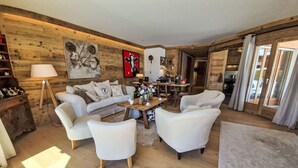 Een gezellige woonkamer met een houten wand, een bank, twee fauteuils, een salontafel en een eethoek op de achtergrond.