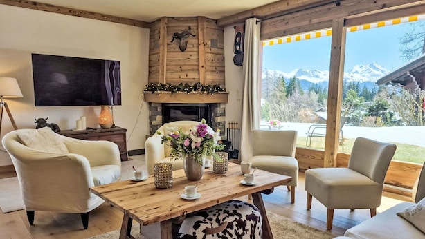 Een gezellige woonkamer met een open haard, comfortabele zitplaatsen, een flatscreen televisie en uitzicht op een berglandschap.