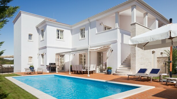 Une maison blanche à deux étages, dotée d’une piscine, d’un espace salon extérieur et d’un patio couvert.