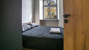 Une chambre à coucher avec un lit, une fenêtre donnant sur des immeubles, une porte et un luminaire.