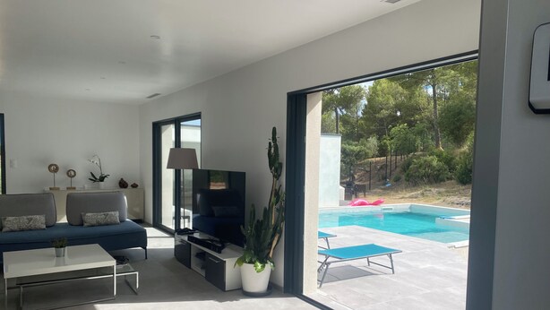 A modern living room with a TV, sofa, coffee table, and a view of an outdoor swimming pool. - Dominant house overlooking pine forest (Les Matelles)