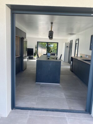 A modern kitchen with a central island, built-in appliances, and a large window providing a view of the outdoors. - Dominant house overlooking pine forest (Les Matelles)