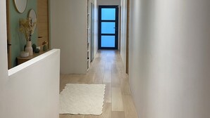 A hallway with a white floor, a white rug, and a door at the end. - Dominant house overlooking pine forest (Les Matelles)