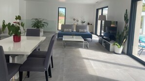 A modern living room with a dining area, a sofa, a TV, and potted plants. - Dominant house overlooking pine forest (Les Matelles)