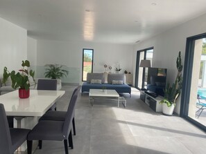 A modern living room with a dining area, a sofa, a TV, and potted plants. - Dominant house overlooking pine forest (Les Matelles)