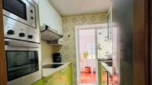 A narrow kitchen with green cabinets, a stainless steel oven, and a refrigerator. - As Casoeiras (O Grove)