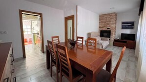 A dining area with a wooden table and chairs, a sofa, a TV, and a fireplace. - As Casoeiras (O Grove)