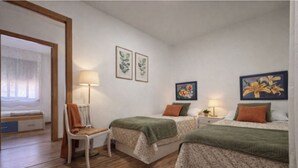 A bedroom with two beds, a chair, a bedside table with a lamp, and wall art. - As Casoeiras (O Grove)