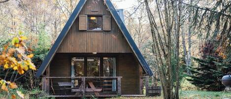 A cabin with a triangular roof, large windows, and a wooden deck.