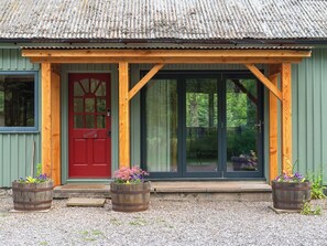Un bâtiment rustique avec une porte rouge, une véranda en bois et de grandes fenêtres.