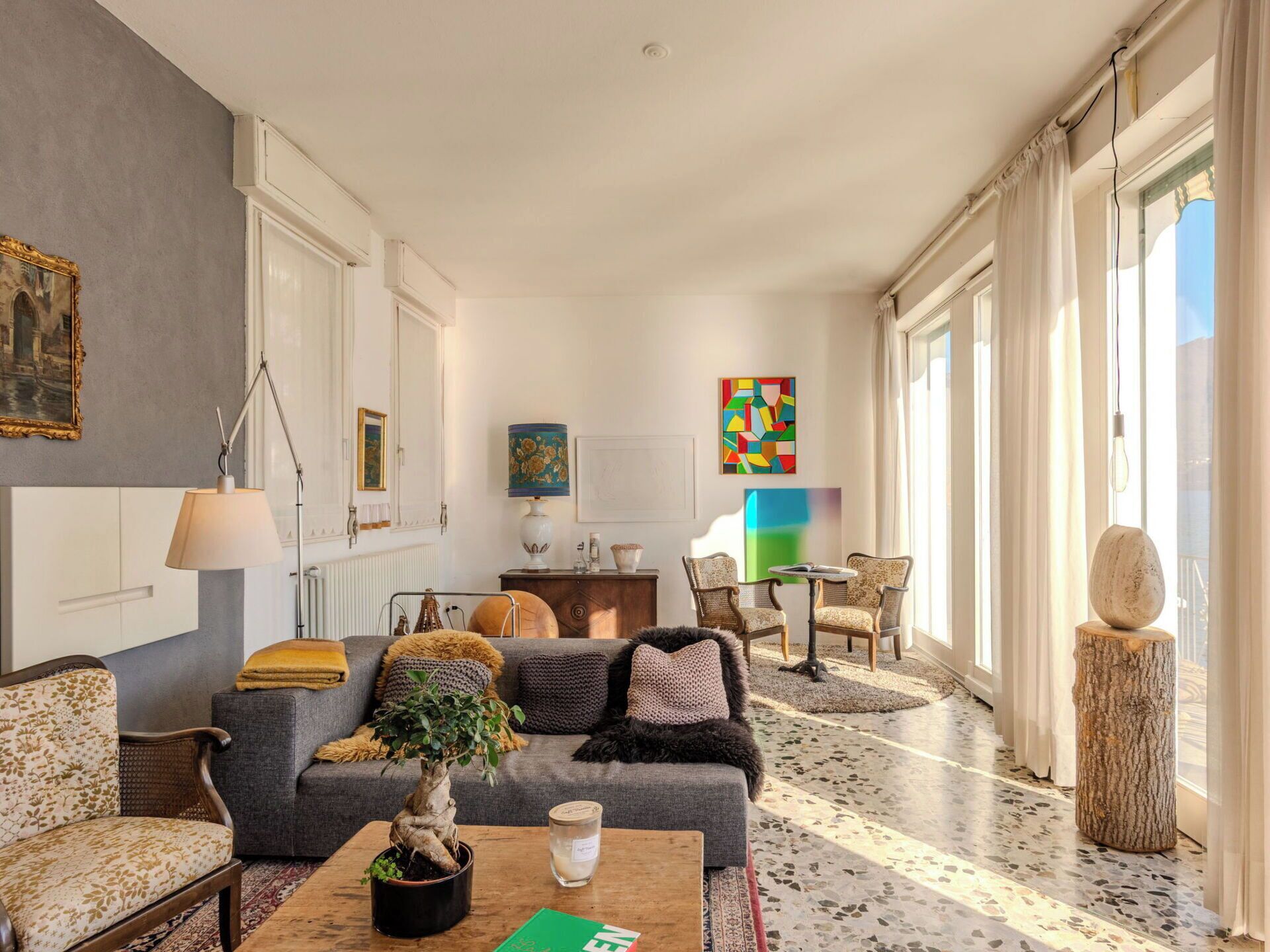 A spacious living room with a sofa, chairs, a coffee table, a potted plant, and artwork on the walls.