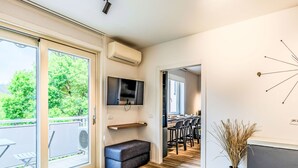 A modern interior with a sliding glass door leading to an outdoor area, a built-in bench, a flat-screen TV, and a dining area with bar stools. - Lovely apartment for 6 guests with A/C, WIFI, TV and patio (Riva Del Garda)