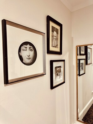 A hallway with framed artwork on the walls and a mirror reflecting the artwork. - Hotel Emerald (Potts Point)