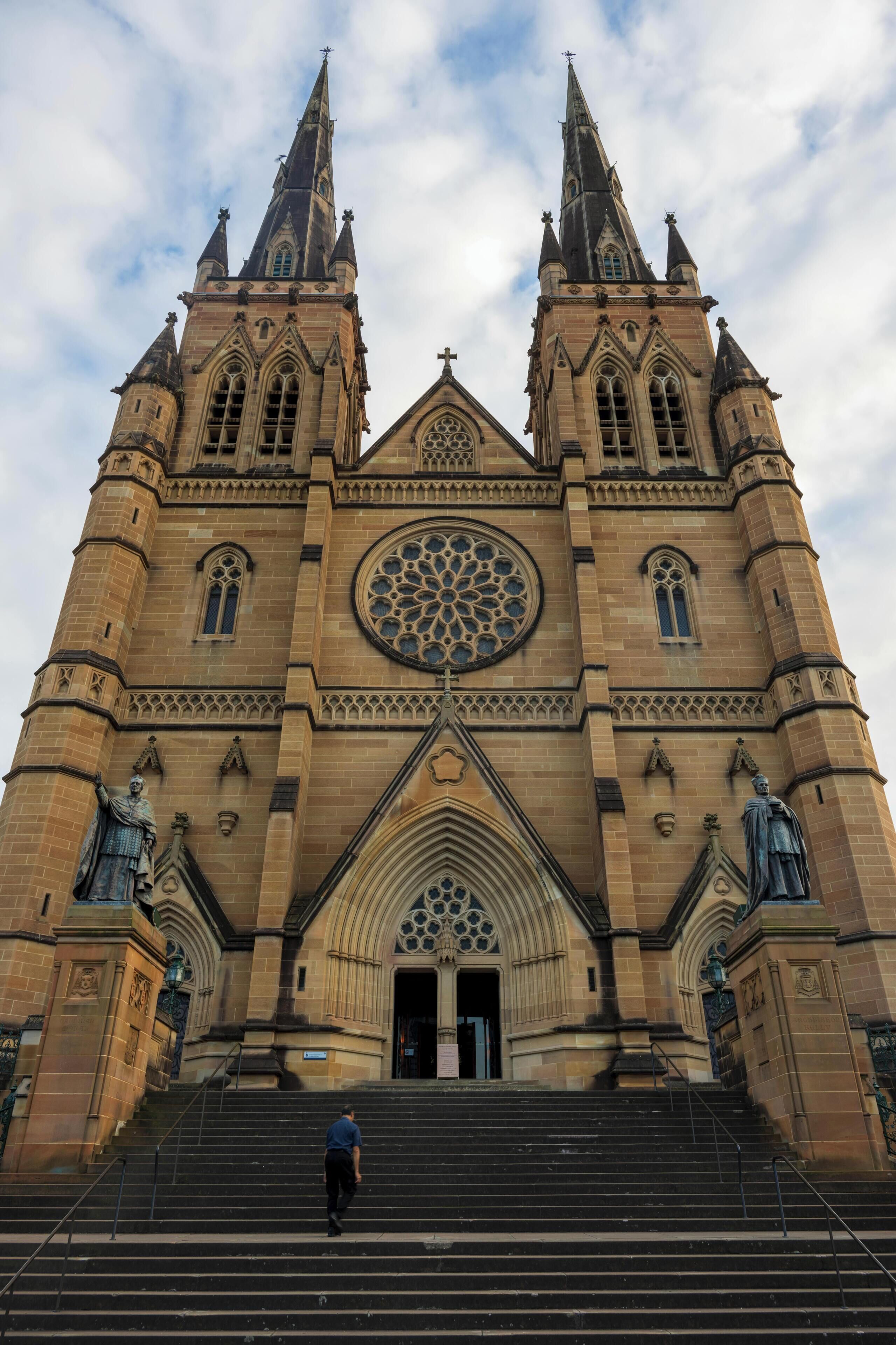 A large cathedral with two tall spires, a large circular window, and a statue at the entrance.