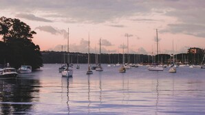 A marina with multiple sailboats docked, calm water, and a backdrop of trees and buildings. - Hotel Emerald (Potts Point)