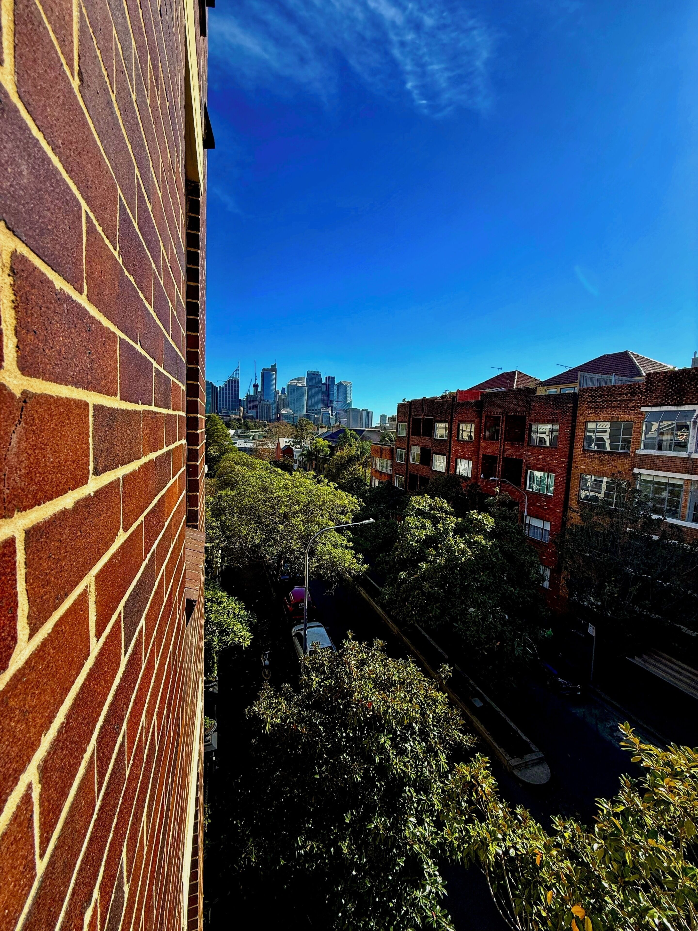 Un edificio alto con fachada de ladrillo y vista del horizonte urbano al fondo.