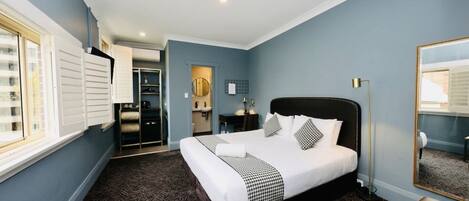 A hotel room with a large bed, a bedside table, a mirror, and a window with blinds.