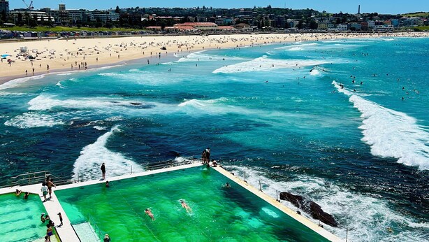 A coastal beach scene with a swimming pool and beachgoers. - Hotel Emerald (Potts Point)