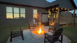 A backyard with a fire pit surrounded by chairs, a covered patio area, and a house with windows. - East TN home with lake views & 2 kitchens (Morristown)