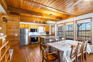 Een houten cabin interieur met een keuken, eethoek en grote ramen.