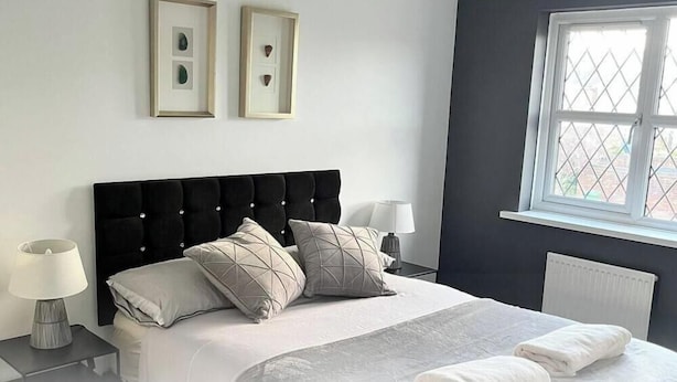 A bedroom with a black headboard, two bedside tables with lamps, a window with a view, and two framed pictures on the wall. - Stylish Stay in Emersons Green + WiFi + Garden (Emersons Green)