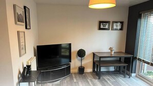 A living room with a flat-screen TV, a small table with a potted plant, and framed pictures on the wall. - Stylish Stay in Emersons Green + WiFi + Garden (Emersons Green)