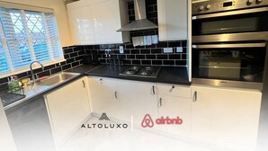 A modern kitchen with white cabinets, black countertops, a stainless steel range hood, and built-in ovens. - Stylish Stay in Emersons Green + WiFi + Garden (Emersons Green)