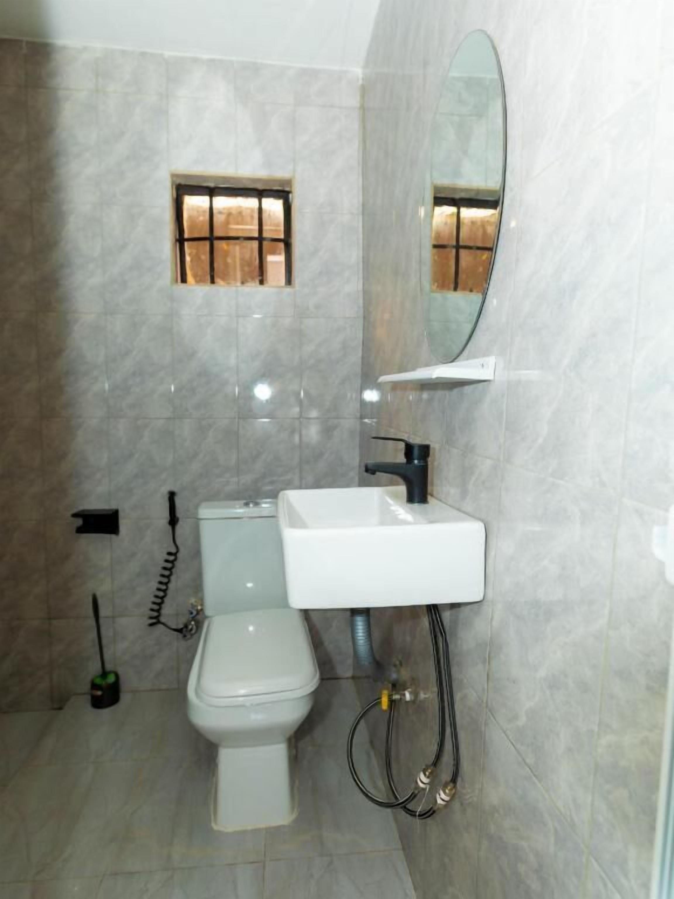 A bathroom with a toilet, sink, mirror, and tiled walls.