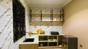 Eine kompakte Küche mit Marmorfliesenspiegel, Spüle, Kühlschrank und Regalen über der Arbeitsfläche.
