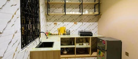Cocina compacta con salpicadero de mármol, pileta integrada, refrigerador y estantes sobre la encimera.