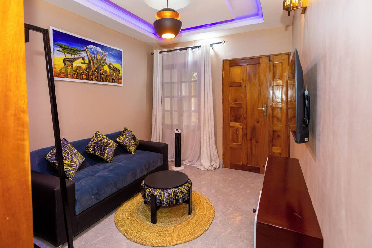 Una sala de estar con un sofá, una mesa de centro redonda, un cuadro, un televisor y una puerta de madera.