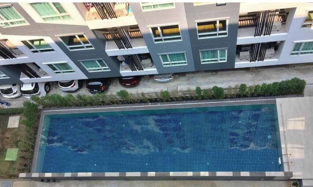 A modern building with a swimming pool, balconies, and parked cars.