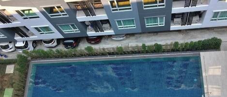 A modern building with a swimming pool, balconies, and parked cars.