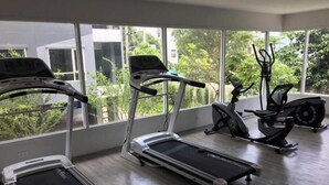 Ein Fitnessstudio mit Laufbändern, einem Crosstrainer und einem Fahrradergometer, große Fenster mit Blick ins Grüne.