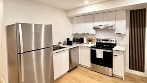 A modern kitchen with stainless steel appliances, white cabinetry, and a wooden floor.