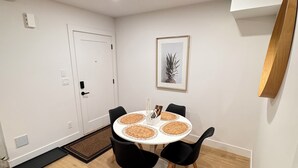 A room with a round table, black chairs, a white door, a framed picture, and a wooden floor.