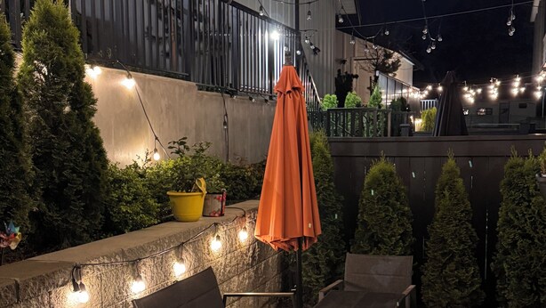 An outdoor patio with tables and chairs, string lights, and a stone wall.