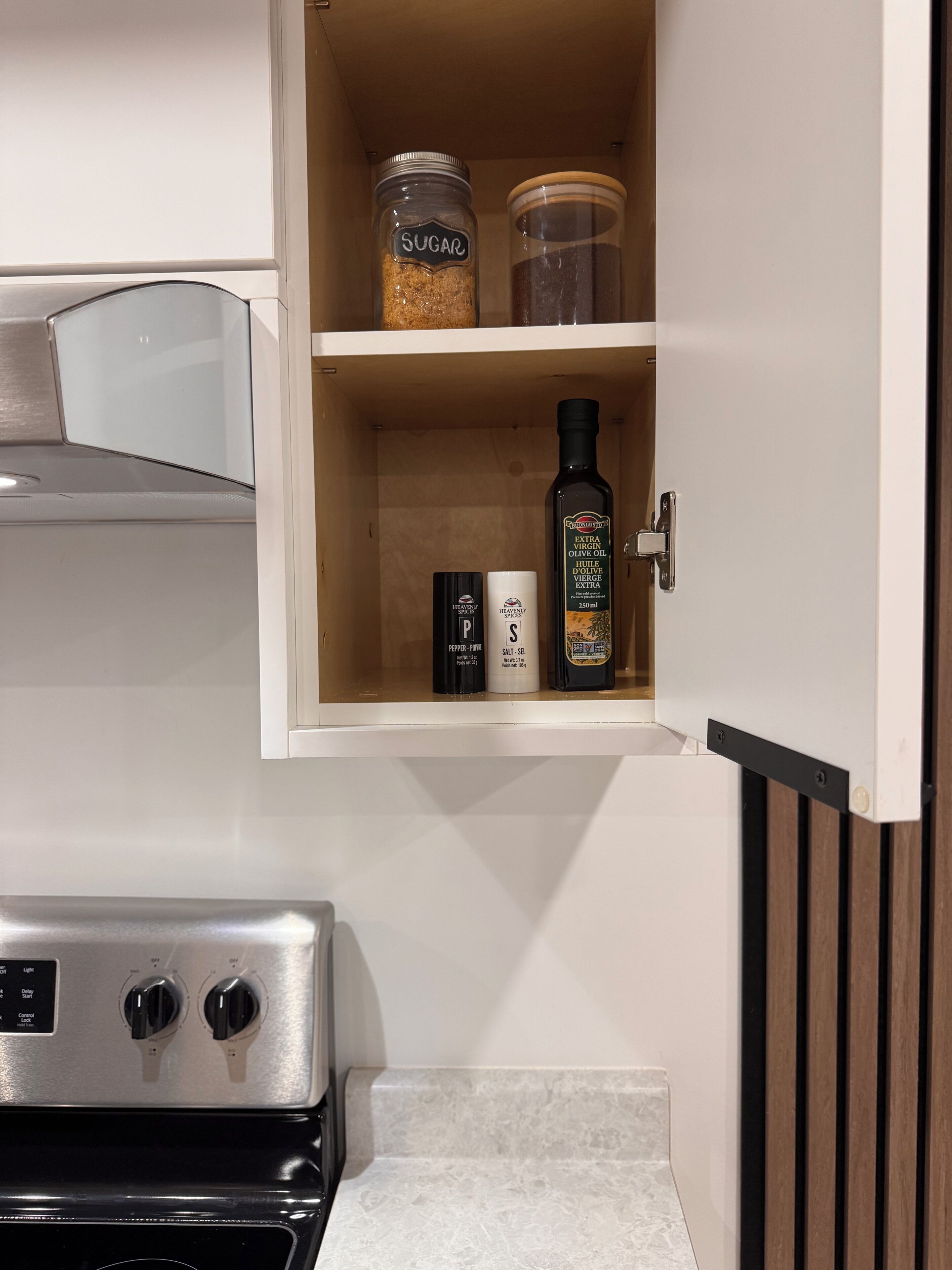 Una cocina con estufa, un armario que contiene azúcar, pimienta y sal, y una botella de aceite de oliva extra.